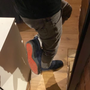 Christian Louboutins - Säljer ett par svarta sneakers från Christian Louboutin med klassisk röd sula. Skorna har snörning och är tillverkade i mocka med diskret broderad logga på hälen. Perfekta för dig som vill ha något stilrent men ändå sticker ut. Skorna har lite slitningar på sig men inget som sticker ut för mycket förutom ett hål i baksidan på ena skon därför kostar skorna endast 850.
