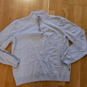 Ljus beige stickad tröja med halv dragkedja från Sand - Säljer en ljusbeige stickad tröja från med halv dragkedja och hög krage. Tröjan har långa ärmar och ribbade muddar vid ärmslut och nederkant. Perfekt för lager-på-lager och stilren look.