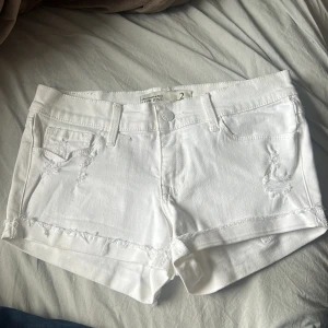 Vita jeansshorts med slitningar - Säljer ett par vita jeansshorts från Mossimo i storlek 2. Shortsen har råa kanter och slitna detaljer framtill, klassisk femficksmodell och bälteshällor. Perfekta för varma dagar och enkel att matcha med allt.