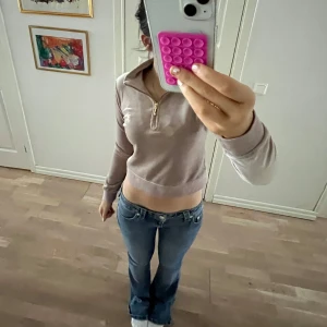 Beige velour hoodie från Juicy Couture - Säljer en snygg beige velour hoodie från Juicy Couture. Tröjan har en dragkedja framtill och ett broderat emblem på bröstet. Perfekt för en avslappnad och stilren look.