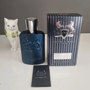 Parfums de Marly layton Royal Essence -  KVITTO FINNS! Elegant parfym från Parfums de Marly i en stilren mörkblå flaska med silverdetaljer. Förpackningen har ett klassiskt randigt mönster och en sköld med hästar. Perfekt för den som söker en lyxig doftupplevelse. Max använd 2 sprut så sprillans ny, säljer då jag behöver pengar.