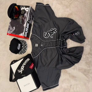 Grå Chicago White Sox baseballtröja från Majestic - Säljer en grå baseballtröja från Majestic med Chicago White Sox-logga på bröstet. Tröjan har knappar framtill, vita kontrastlinjer och är tillverkad i ett syntetmaterial. Perfekt för dig som gillar sportig stil.
