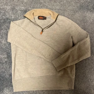 Beige merinoulltröja med dragkedja från Morris - Säljer en stilren beige tröja från Morris i 100% merinoull. Tröjan har en liten dragkedja vid kragen och diskret broderad logga på bröstet. Perfekt för lager-på-lager och snygg till både jeans och chinos. Lite mindre i storlek för den är  tvättad 