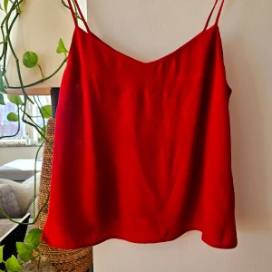 Röd linnetopp med tunna axelband - Säljer en röd linnetopp från H&M med tunna axelband och v-ringad hals. Perfekt för varma dagar eller som lager under en kavaj. Enkel och stilren design i mjukt material.