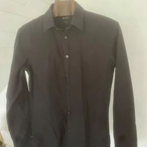 Svart skjorta från Tiger of Sweden - Säljer en stilren svart skjorta från Tiger of Sweden i slim fit-modell. Skjortan har klassisk krage, långa ärmar och knäppning framtill. Perfekt för dig som gillar en smalare passform och vill ha en tidlös look.