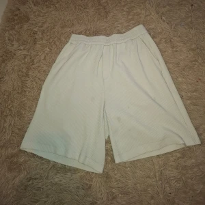 Vita ribbade shorts från SWAG DESIGN - Säljer ett par vita shorts från SWAG DESIGN med diskret ribbad struktur plus några fläckar. De har elastisk midja och en bakficka. Perfekta för varma dagar och har en avslappnad passform.