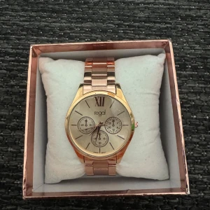 Roséguldfärgad klocka från Regal - Stilren klocka i roséguld från Regal med metallarmband och stor urtavla. Aldrig använt! 