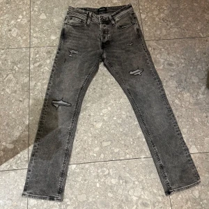 Jack & Jones jeans - Säljer ett par gråa Jack & Jones jeans med slitningar på låren och knäna. klassisk femficksdesign och normal passform. Perfekta för en avslappnad och najs look.