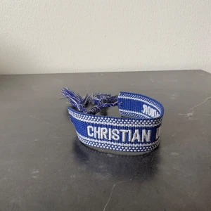 Blått armband från Dior - Säljer ett blått armband från Dior. Armbandet har justerbar knytning med fransar i ändarna. Perfekt accessoar för att lyfta din outfit.