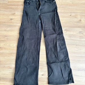 Svarta/mörk-grå wide leg jeans från Divided - Säljer ett par svarta/mörk-grå jeans från Divided med wide leg-passform. Byxorna har klassisk femficksdesign, dragkedja och knapp framtill. Perfekta för dig som gillar en avslappnad och trendig stil.