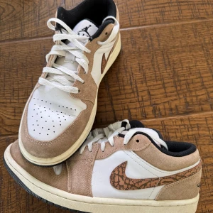 Air Jordan 1 Low SE Brown Elephant - Säljer ett par Air Jordan 1 Low SE Brown Elephant med beige mocka och vit läderbas. Swooshen har ett unikt brunt mönster och skorna har vita snören samt svart innersula. Sparsamt använda och i mycket gott skick. Storlek 42. 