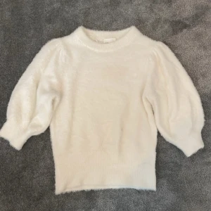 Vit stickad tröja med puffärmar - Superfin vit stickad tröja med puffiga ärmar och ribbade muddar. Perfekt för att ge en söt och trendig look till din outfit. Mjuk och skön med rund halsringning.