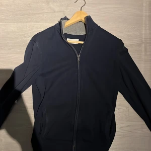 Mörkblå ziptröja från Pier One str XS/S - Mörkblå ziptröja från Pier One med ribbad krage och hel dragkedja framtill. Jackan har två fickor på sidorna och är tillverkad i mjukt material som känns bekvämt. Perfekt för lager-på-lager under kyliga dagar.