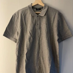 Grå pikétröja från J.Lindeberg  - Snygg grå pikétröja från J.Lindeberg i storlek XXL. Klassisk modell med krage, knappar framtill och diskret logga på bröstet. Perfekt till jeans eller shorts för en clean look. Pris kan diskuteras 