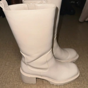 Beiga chunky boots med klack - Snygga boots i beige skinn med chunky sula och låg klack. Högt skaft och rund tå ger en cool och modern look. Perfekta för dig som vill sticka ut med stilrena men trendiga skor.