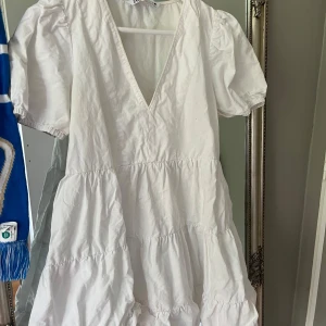 Vit kort klänning från Zara XS - Supersöt vit kort klänning från Zara med puffärmar och v-ringning. Klänningen har volanger i flera lager och en luftig passform som känns perfekt för varma dagar. Enkel och stilren design som är lätt att matcha med sneakers eller sandaler. Perfekt nu till sommaren 