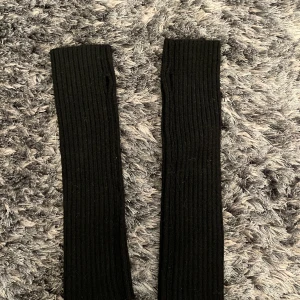 Svarta ribbstickade handledsvärmare - Säljer ett par svarta, ribbstickade handledsvärmare med tumhål. Perfekta att dra på sig när det är kallt ute och du vill ha händerna fria men ändå hålla värmen. De är långa och sitter tajt runt handleden och underarmen. Helt nya, oanvända🤍