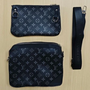svart axelväska monogram - Säljer en svart axelväska med klassiskt monogrammönster i grått. Väskan har två delar, båda med dragkedja och avtagbar axelrem med logga. Tillverkad i skinn med silverfärgade metalldetaljer. Perfekt för att bära det viktigaste med stil.
