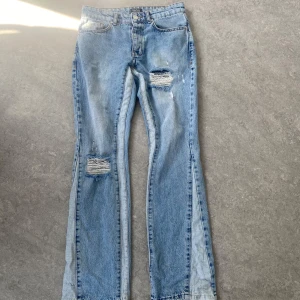 Ljusblå bootcut jeans med slitningar - Säljer ett par ljusblå bootcut jeans från MAN med snygga slitningar på knäna. Jeansen har klassisk femficksdesign, hög midja och är tillverkade i jeansmaterial. Perfekta för dig som gillar en avslappnad och trendig look.