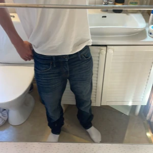 Mörkblå jeans från Jack & Jones - Säljer ett par mörkblå jeans från Jack & Jones med snygga slitningar och klassisk femficksdesign. Jeansen har normal passform och raka ben, perfekt för en avslappnad stil. Materialet är mjukt och bekvämt denim i bomull.