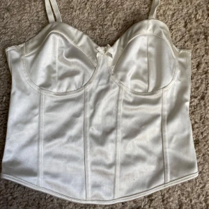 Vit korsettopp från H&M - Snygg vit korsettopp i satin från H&M💗Toppen har bygelkupor, justerbara axelband och en liten rosett framtill. Pris går att diskutera!!💗