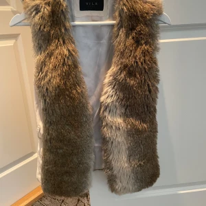 Brun pälsväst från VILA - Säljer en brun fusk pälsväst från VILA i storlek S. Västen har mjukt fuskpälsmaterial på utsidan och slät insida. Perfekt för att lyfta din outfit med en trendig touch. Färgen är naturligt brun med lite skiftningar.
