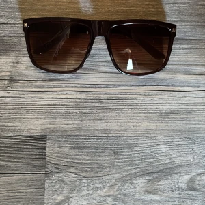 Raybans boyfriend liknande  - Snygga solglasögon med svart, glansig båge och fyrkantig form. Glasen är mörktonade i brunt och ger en cool vibe. Perfekta för att lyfta din stil under soliga dagar.