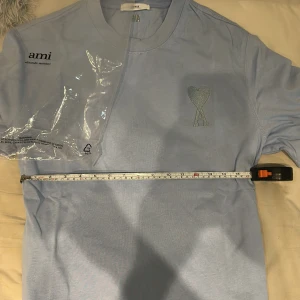 Ljusblå t-shirt från Ami Paris - Snygg ljusblå t-shirt från Ami Paris med klassisk passform. T-shirten har korta ärmar, rund halsringning och ikoniskt broderat hjärta med A på bröstet. Tillverkad i mjuk bomull som känns skön mot huden. Perfekt för en clean och stilren look. Säljer pågrund av att den ejj passar mig (för stor) och endast swish gäller. 