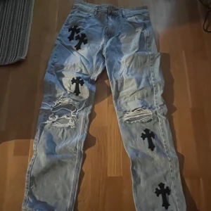 Ljusblå jeans med svarta kors från Mennace - Unika ljusblå jeans från Menace med svarta kors och slitna detaljer på benen. Liknar chrome hearts jeans. 