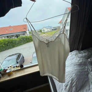 Vit linnetopp med spetsdetaljer - Supersöt vitt linne med spets längs urringningen. Perfekt för lager-på-lager eller som statement-piece. Aldrig använd