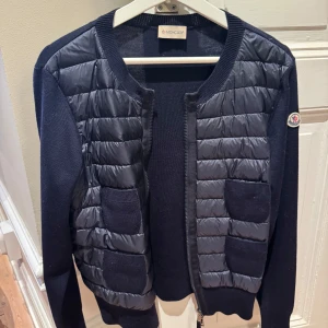 Moncler Cardigan - Moncler cardigan med quiltad, glansig front och två fickor. Ärmar och rygg är stickade, och ärmen har Moncler-logga. 