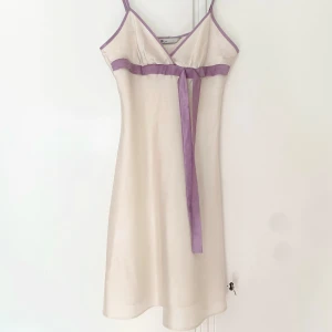 Sidenklänning med lila rosett - Superfin kort klänning i champagnefärgad satin från Bay. Smala axelband, v-ringad och lila kantband samt en söt lila rosett under bysten. (Är inte så värst bra på att knyta rosett haha) Priset kan diskuteras