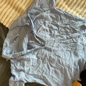 Ljusblå skjorta från Hollister - Ljusblå skjorta från Hollister med klassisk krage och knappstängning framtill. Bröstficka med röd broderad logga. Läs bio!💕