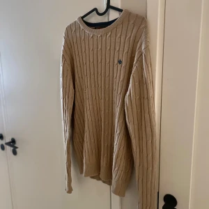 Beige kabelstickad tröja Morris - Beige stilren Kabelstickad tröja från Morris med diskret logga broderad på bröstet. Tröjan har långa armar, rund halsringning. Klassisk och stilren design som funkar till det mesta. Storlek M passar M. Toppskick! Inga tecken på användning! Nypris 1599:- mitt pris endast 399:- och fri frakt!