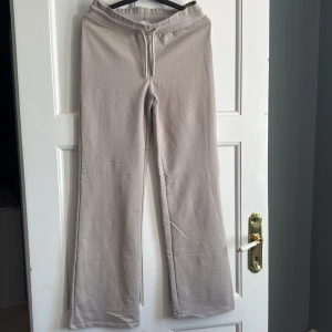 Beige mjukisbyxor från 157, storlek M - Beiga mjukisbyxor från 157 med dragsko i midjan och raka, lite vidare ben. Byxorna är tillverkade i mjukt bomullsmaterial och har en enkel, clean look utan synliga loggor eller detaljer. Perfekta för en chill och avslappnad stil.