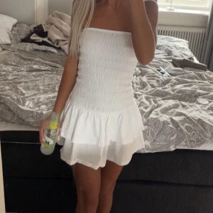 Vit axelbandslös kortklänning - Supersöt vit kortklänning med smockad överdel och volangig kjol. Axelbandslös modell som ger en fräsch och somrig vibe. Perfekt för varma dagar och snygg att styla med sneakers eller sandaler. Helt ny endast testad men tyckte inte den passa mig