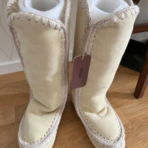Beige mockaboots från Mou, stl 39 - Snygga beige boots från Mou i mjuk mocka med grov stickad kant runt skaftet och sulan. Höga och varma med platt sula, perfekta för kyliga dagar. Klassisk Mou-logga bak på hälen och vågig yttersula för bra grepp.