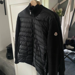 Svart cardigan från Moncler  - Storlek S men passar även riktigt bra på storlek M Snygg svart cardigan från Moncler med quiltad framsida och släta ärmar. Jackan har hög krage, dragkedja framtill och två dragkedjefickor. Moncler-logga på ena ärmen. Perfekt för dig som vill ha en stilren och sportig look.