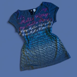 Hello Kitty topp - Grå kortärmad topp från H&M med Hello Kitty-tryck i flera färger över hela framsidan. Trycket går i rosa, vitt, blått och turkost och ger en cool gradient-effekt.