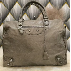Balenciaga weekender väska - Säljer en stor grå handväska från Balenciaga i mjukt skinn. Väskan har flätade handtag, silverfärgade metalldetaljer och en dragkedja framtill. Klassisk design med coola nitar och snygga sömmar. Perfekt för dig som gillar statement-väskor.