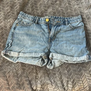 Ljusblå jeansshorts från Lindex - Snygga ljusblå jeansshorts från Lindex med klassisk femficksdesign och uppvikta benslut. Shortsen har gylf med dragkedja och knapp, samt läderpatch med Detroit-logga bak. Perfekta för varma dagar och enkel att matcha med allt.