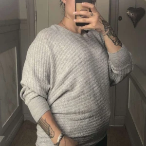 Ljusgrå ribbad stickad tröja - Mysig ljusgrå stickad tröja med ribbad struktur och långa ärmar. Tröjan har en relaxed fit och breda muddar vid ärmsluten. Perfekt för lager-på-lager och chill dagar.