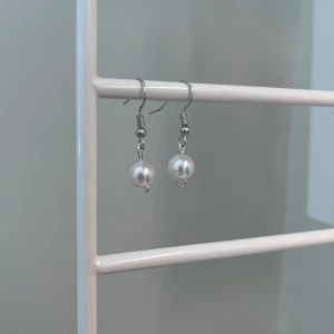 Silvriga örhängen med pärlor - Stilrena örhängen med silverfärgade krokar och vita pärlor som hänger ned. Perfekta för att ge en klassisk touch till din look. Enkla att matcha och lätta att bära.