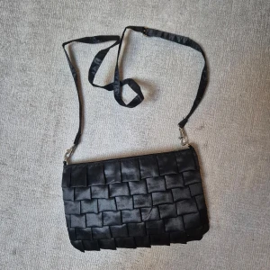 Svart väska från Gina Tricot - Snygg svart, glansig väska från Gina Tricot. Väskan har en avtagbar axelrem och kan användas som kuvertväska. Stängs med dragkedja. Perfekt storlek för det viktigaste till festen med en stilren look.