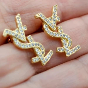 örhängen med strass - Snygga YSL örhängen i guld med glittrande strass-stenar. Ikonisk logga i en cool design som verkligen sticker ut. Perfekta för dig som vill ha något extra och älskar statement-smycken.