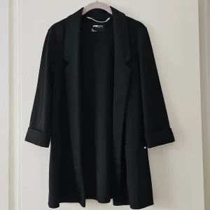 Svart kavaj från FB Sister - Säljer en svart kavaj från FB Sister i storlek M. Kavajen har lång ärm med uppvikta muddar, klassisk krage och öppen front. Perfekt för en stilren och enkel look.