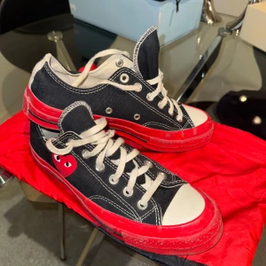 Svarta sneakers med röd sula och hjärtdetalj - Svarta låga sneakers med vit tå och röd sula från Converse i samarbete med Comme des Garçons Play. Skorna har vit snörning, tydliga kontrastsömmar och den ikoniska röda hjärtdetaljen på sidan.