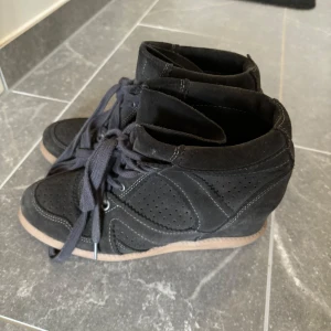 Svarta sneakers med kilklack - Säljer ett par svarta sneakers med kilklack och snörning. Skorna har perforerade detaljer på sidorna och en ljusbrun sula. Perfekta för dig som vill ha en sportig look med lite extra höjd. Påminner om Isabel marant💕 Pris kan diskuteras!!💗