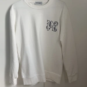 Vit sweatshirt från Palm Angels - Säljer en vit sweatshirt från Palm Angels med svart tryck på bröstet och stor logga på ryggen. Tröjan har rund halsringning och långa ärmar. Perfekt för dig som gillar streetwear och vill sticka ut med en snygg logga.storlek L men sitter rätt så slim. Tröjan är inte äkta