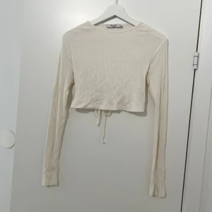 Vit topp med öppen rygg - Naturvit långärmad topp med ribbad struktur,  croppad passform och öppen rygg. Använd 1 gång. 